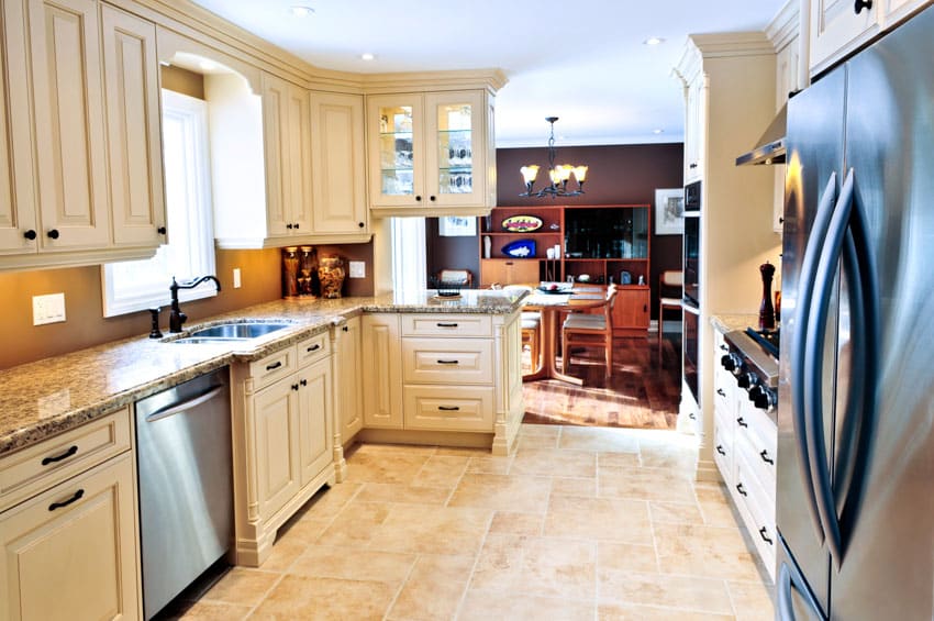Vintage kitchen with white cabinets, dishwasher, windows, travertine tile floor, countertops, and refrigerator