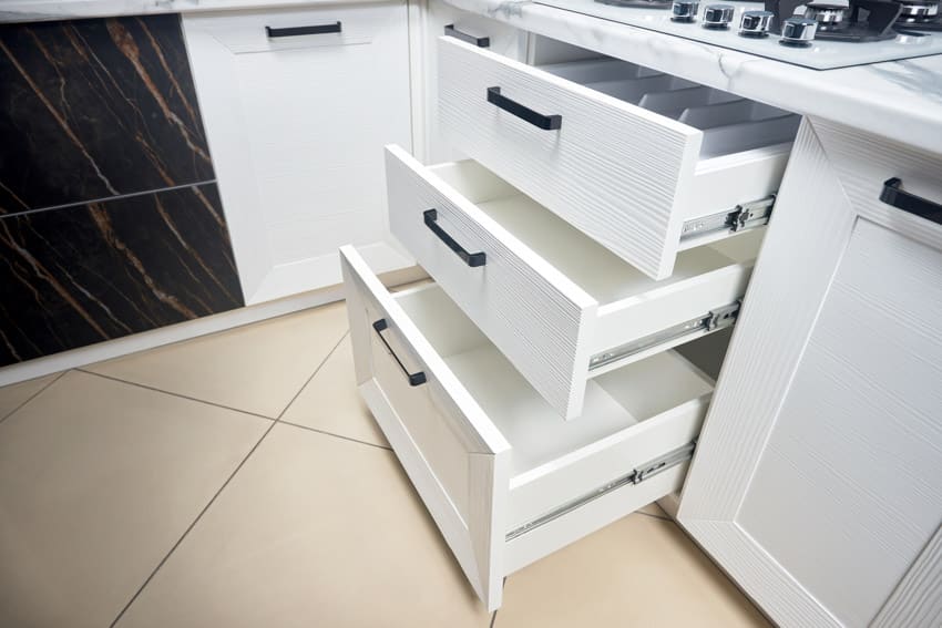 White kitchen with different drawers, slides, open tile flooring, and cabinets