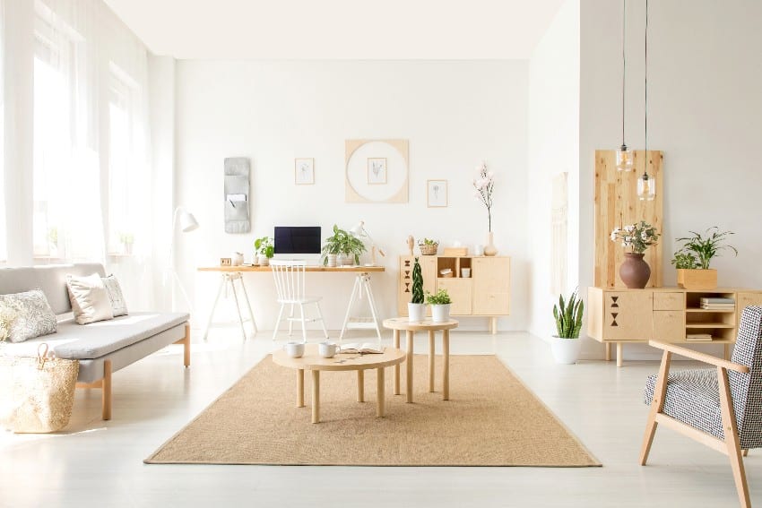 Wooden table on brown carpet between sofa and armchair in white open space interior
