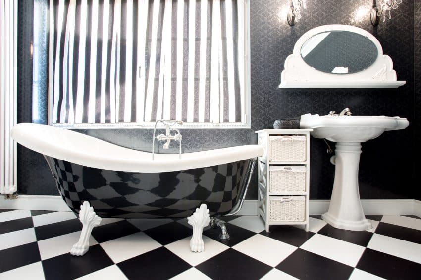 Unique bathroom interior features black and white square tiles, bathtub and stone pedestal sink