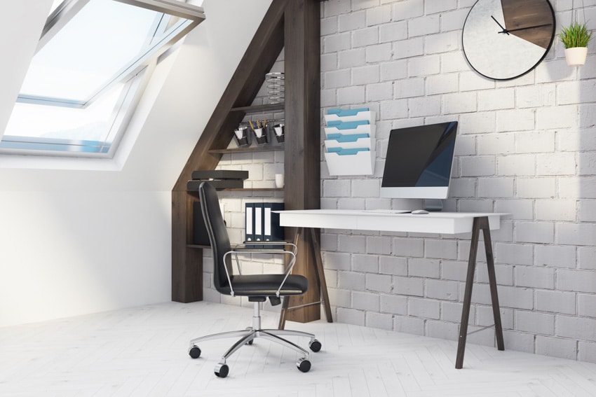 Attic office with desk, computer, brick wall, skylight window, and wall clock