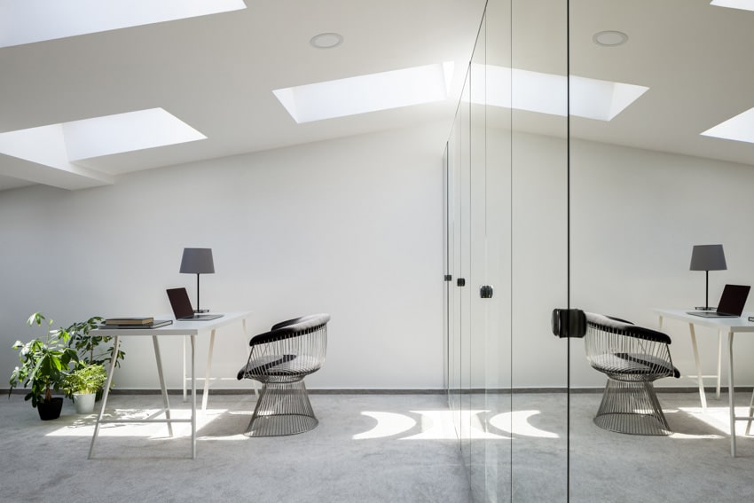 Attic office with mirrored wall, desk, chair, lamp, indoor plant, and skylight windows