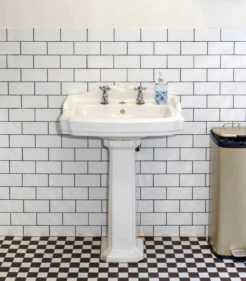 Bathroom features white porcelain vintage pedestal sink with double tap and white subway tiles on the wall
