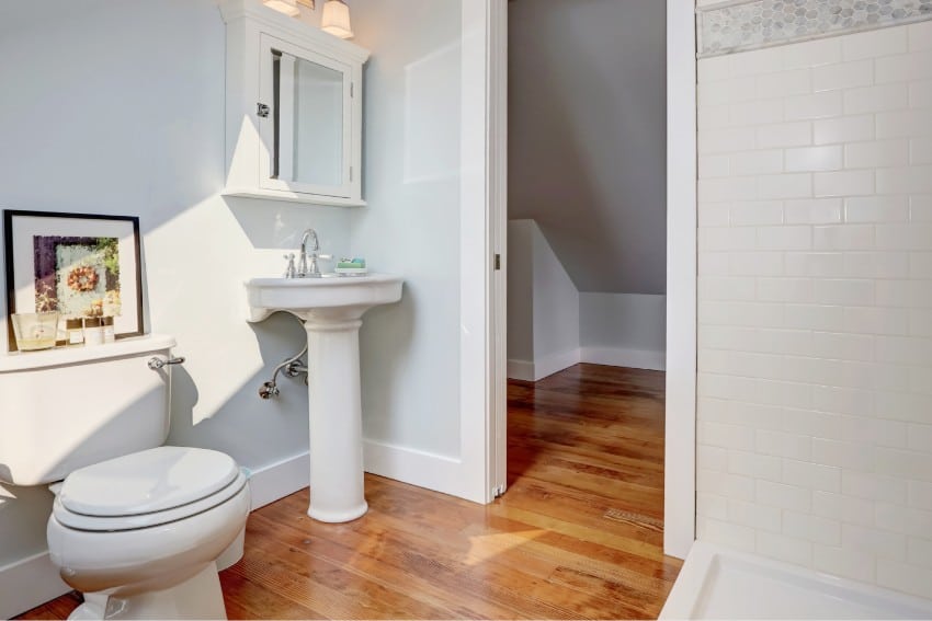 Bathroom with a corner pedestal sink, a toilet, white tile, pastel blue walls and hardwood floors