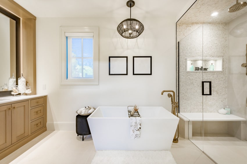 Bathroom with bathtub, vanity mirror, countertop, cabinets, mirror wall, pendant light, window, and bathtub faucet