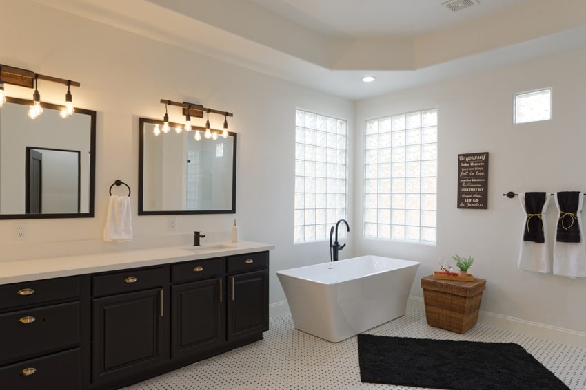 Bathroom with glass block windows, tub, cabinets, countertop, mirrors, and lighting fixtures