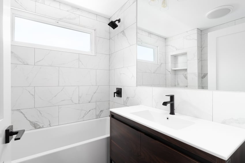 Bathroom with marble tile wall, frosted glass window, sink, countertop, tub, and vanity mirror