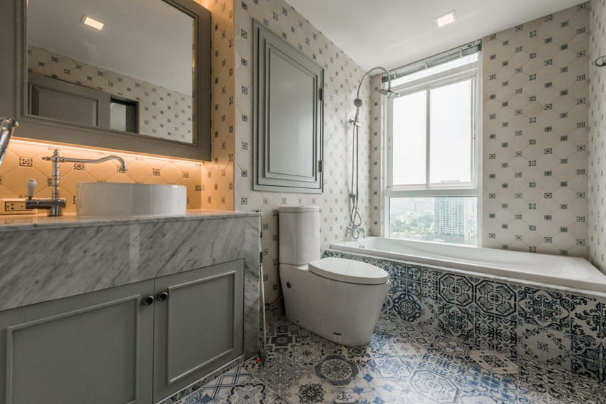 Bathroom with octagon tile wall, Spanish tile floors, tub, toilet, cabinets, vanity mirror, sink, faucet, and window