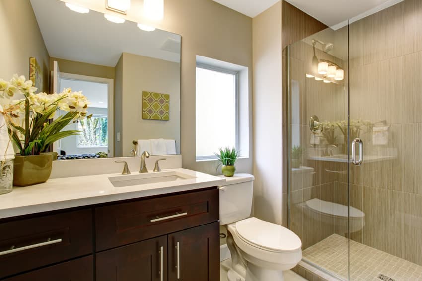 Bathroom with tempered glass window, toilet, glass door, shower, countertop, cabinets, and vanity mirror