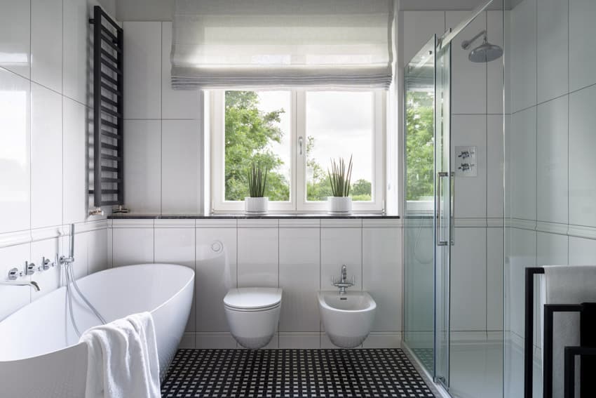 Bathroom with tub, casement windows, glass shower enclosure, toilet, bidet, towel holder, and vertical tile wall
