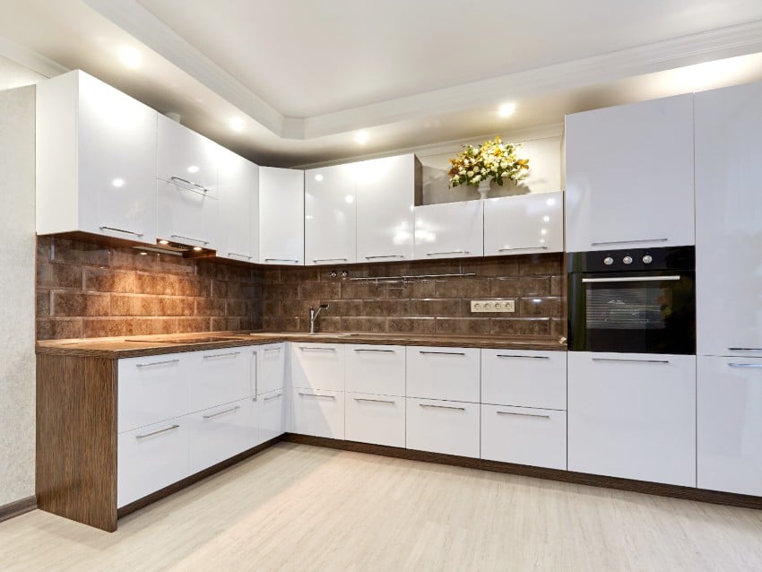 Beautiful fitted kitchen interior with appliances, white cabinets, granite backsplash and vinyl floors