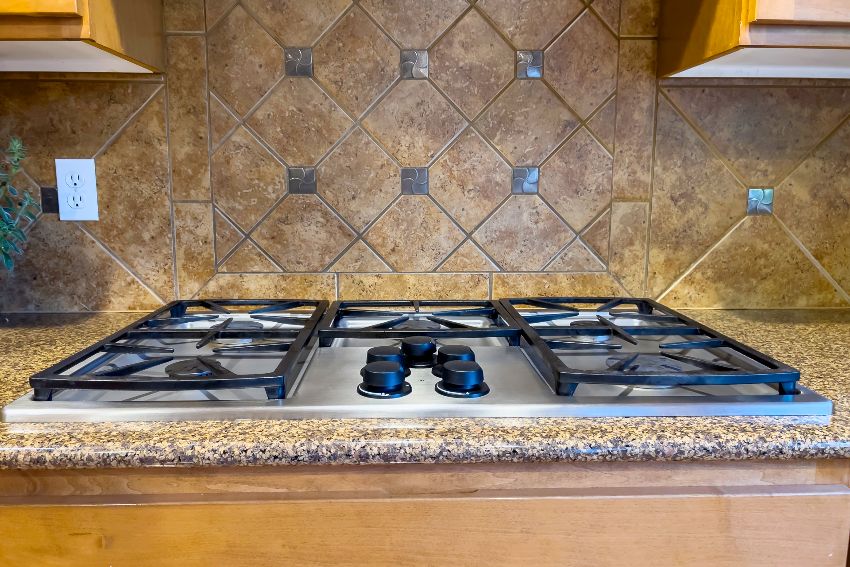 Beautiful gas stove top with black knobs against a terracotta tile backsplash