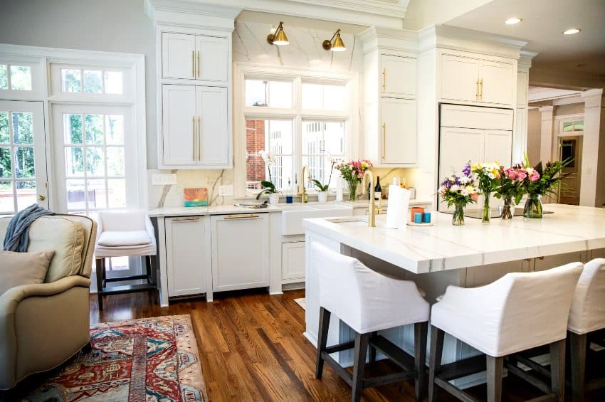 Beautiful kitchen features white kitchen cabinets with legs, island with chairs and hardwood floors