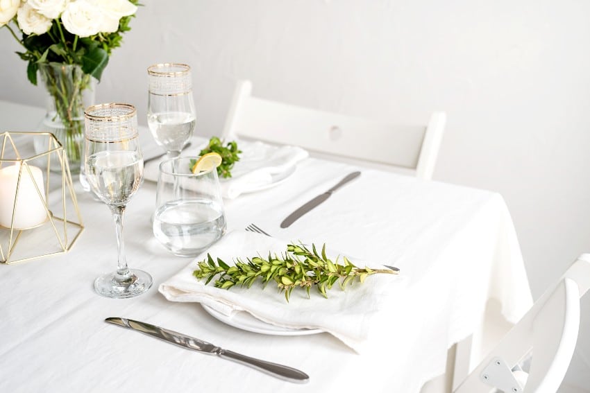 Beautiful table setting for romantic dinner for two with linen napkins, white roses and boxwood