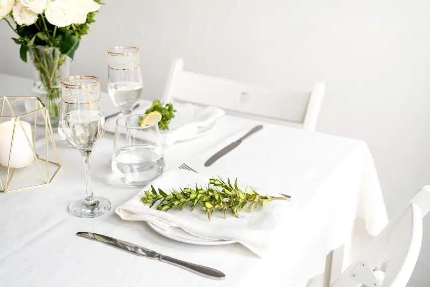 Beautiful table setting for romantic dinner for two with linen napkins, white roses and boxwood