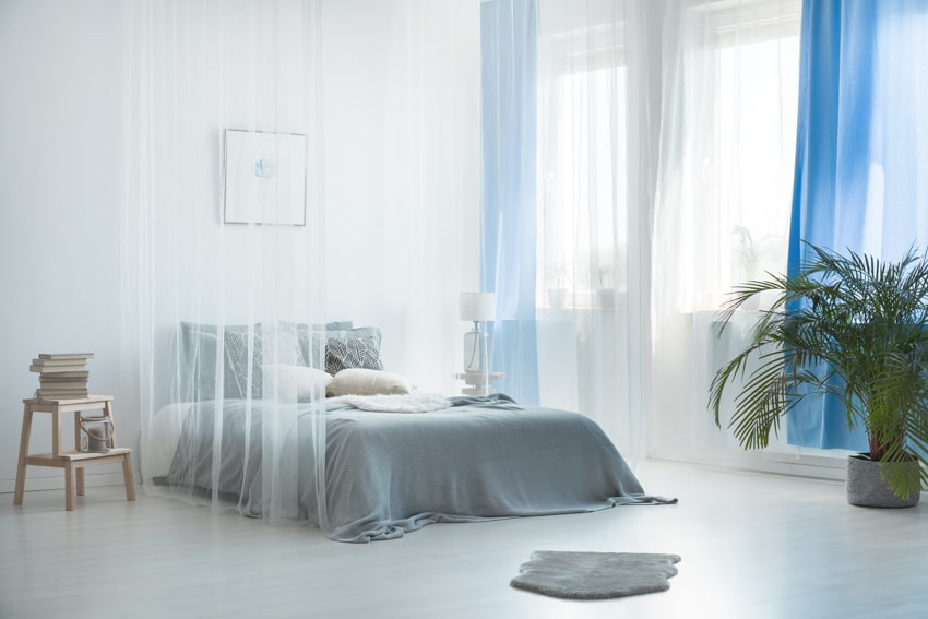 Bedroom with pale light blue wall, bedding, pillows, customized wood nightstand, and indoor plant