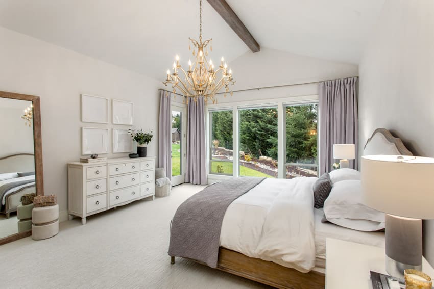 Bedroom with shaker furniture, dresser, chandelier, pillows, mattress, lamp, mirror, glass door, and curtains