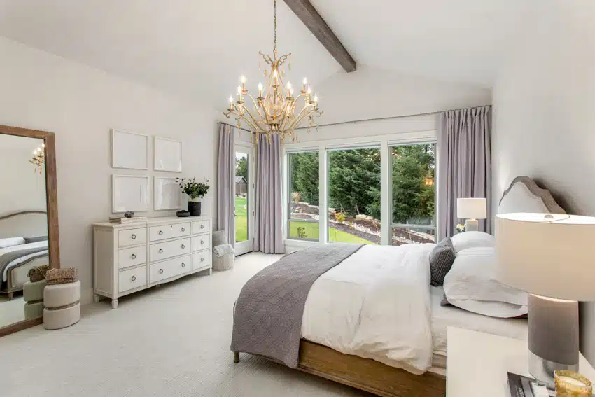 Bedroom with chandelier, periwinkle curtains, white bed sheets and tall mirror