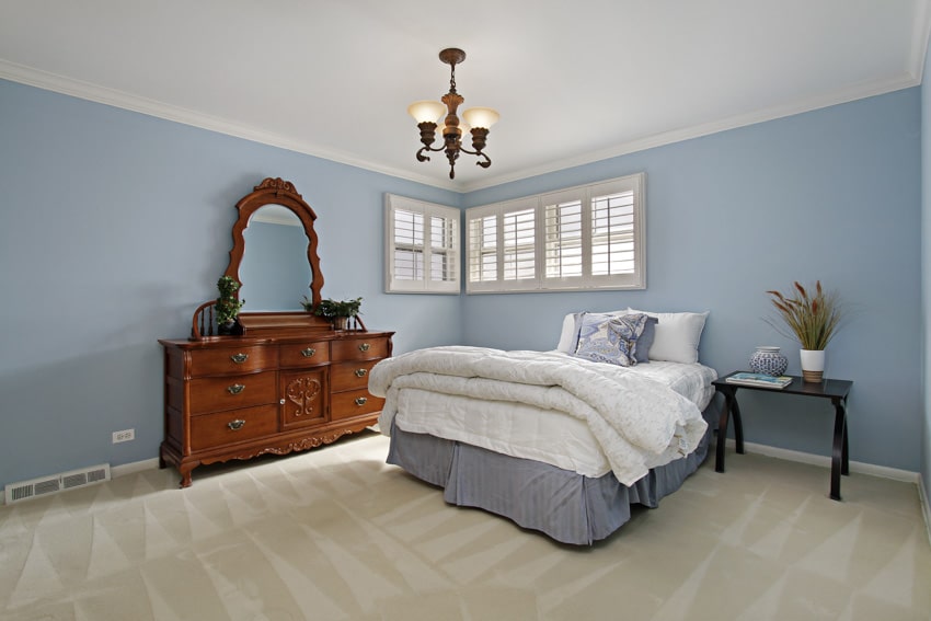 Bedroom with sky light blue wall, bedding, pillows, vanity mirror, dresser, pendant light, nightstand, and window