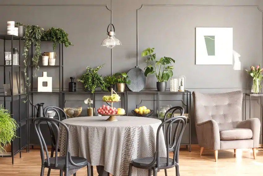 Black chairs at round table with gray tablecloth and fruits in loft interior with armchair next to flowers