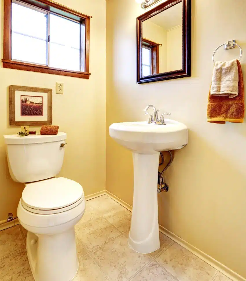Bright beige bathroom interior with old pedestal sink, toilet, and tile floor