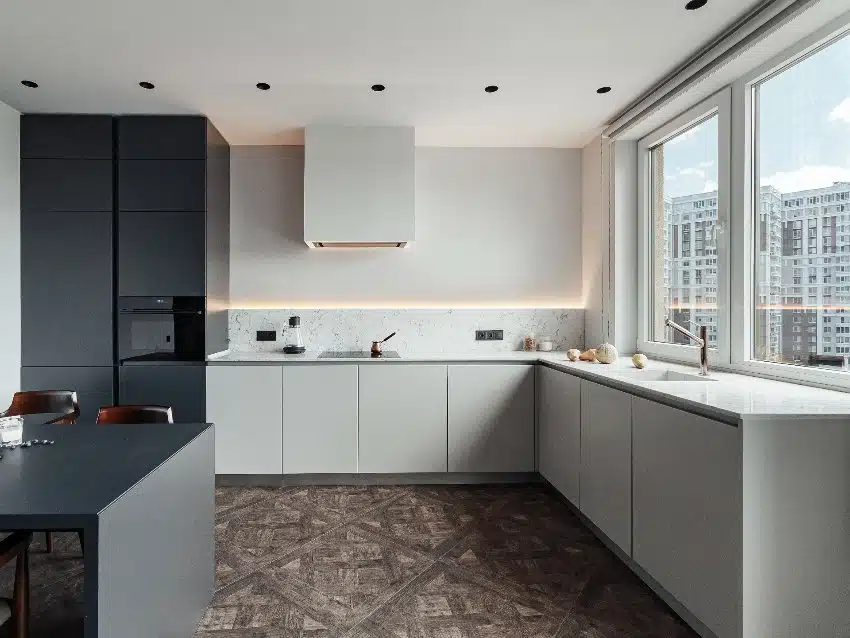 Bright L shaped fitted kitchen design with dark table accessories and equipment, white walls, marble working surface and parquet floor