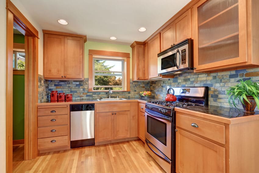 Classic kitchen with faux stacked stone backsplash, wood cabinets, countertop, window, oven, and ceiling lights