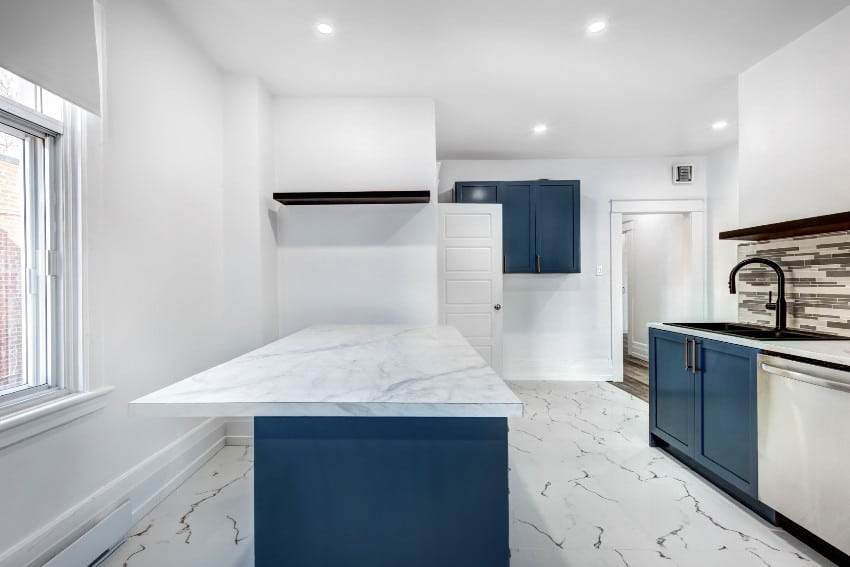 Kitchen with blue island and under faucet cabinets, marble flooring and white walls