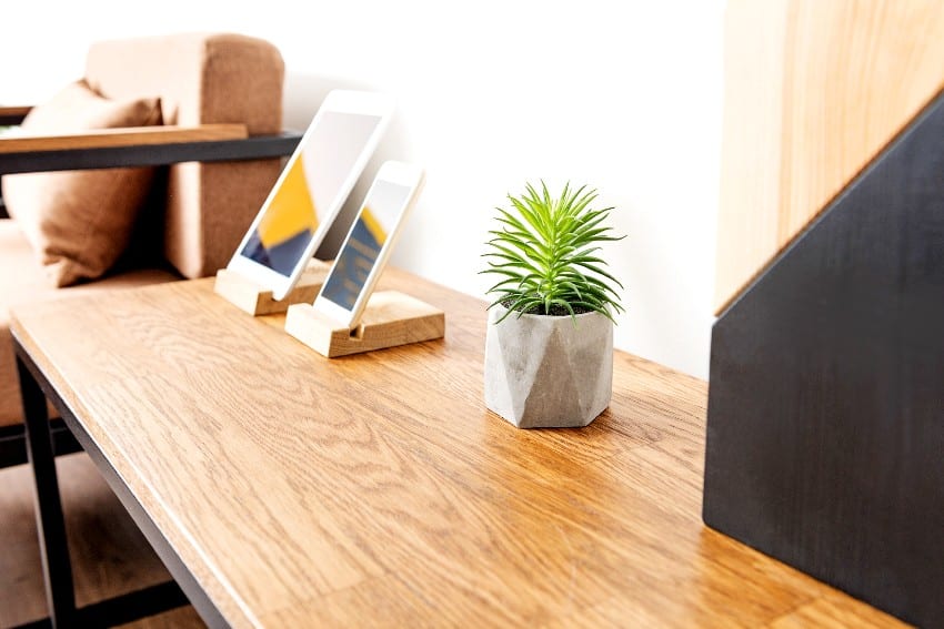 Close up of chestnut wood table surface with smart phone, tablet and little planter with domestic flower in it