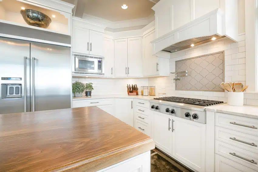Contemporary kitchen with arabesque tile backsplash, white cabinets, range hood, wood countertop, and refrigerator
