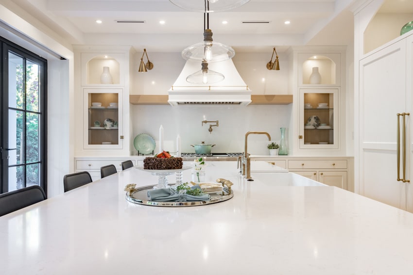 Contemporary kitchen with range hood, marble countertop, pendant lights, glass cabinets, chairs, windows, and white laminate backsplash