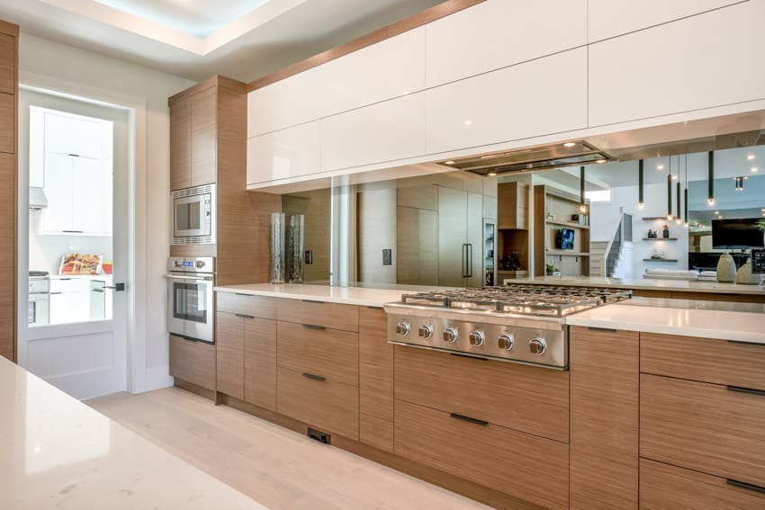 Contemporary kitchen with tinted mirror backsplash, white cabinets, wood drawer, countertop, stove, and glass door