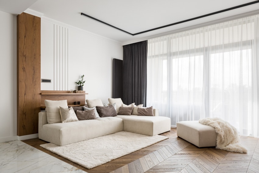Contemporary living room with carpet mat, sectional sofa, ottoman, wood accent wall, window, and curtains