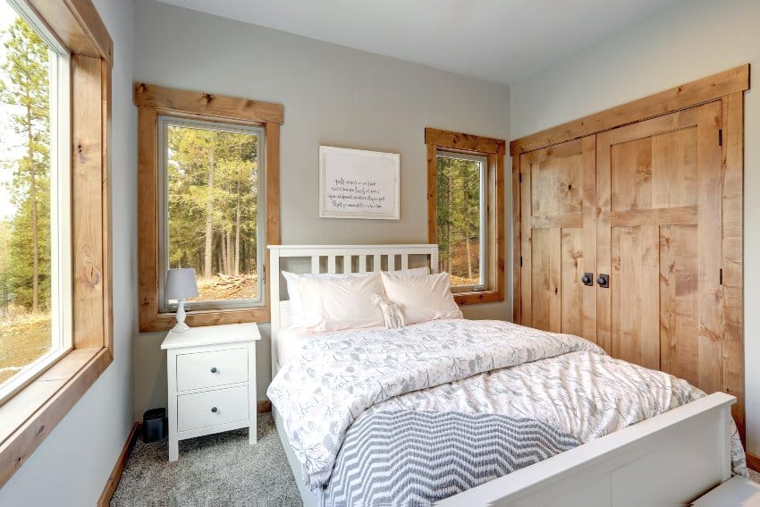 Cozy cottage style bedroom interior features wooden closet doors, white bed with headboard, pale pink and gray bedding
