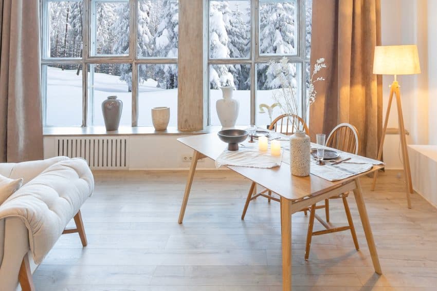 Cozy warm home interior of a chic country chalet with white alder furniture and huge panoramic window overlooking the winter forest