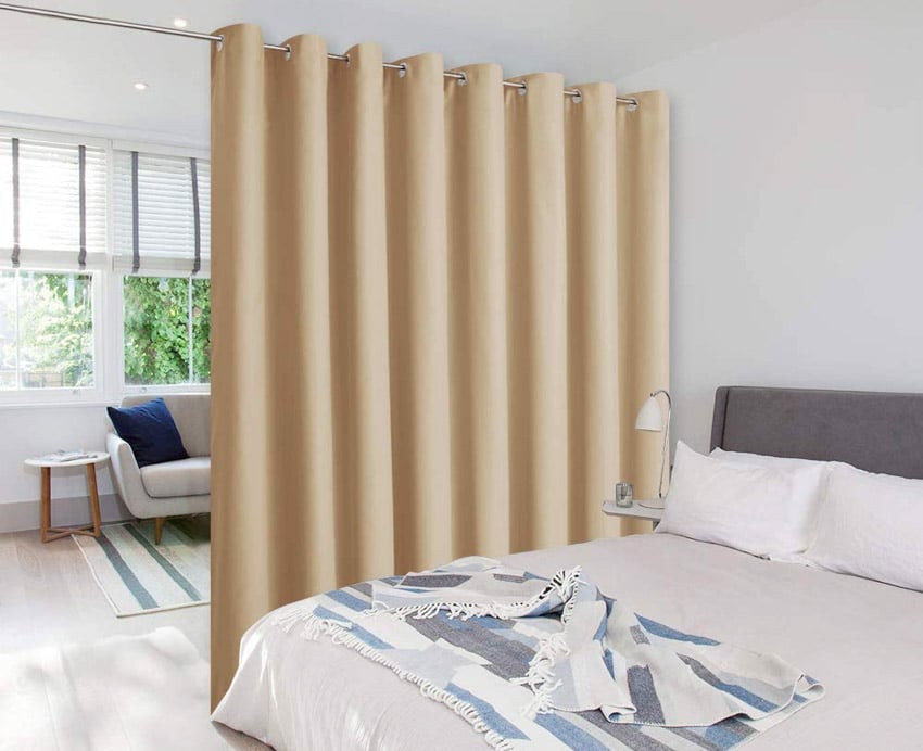 Curtain divider for studio units with comforter, pillows, lamp, couch, side table, and window