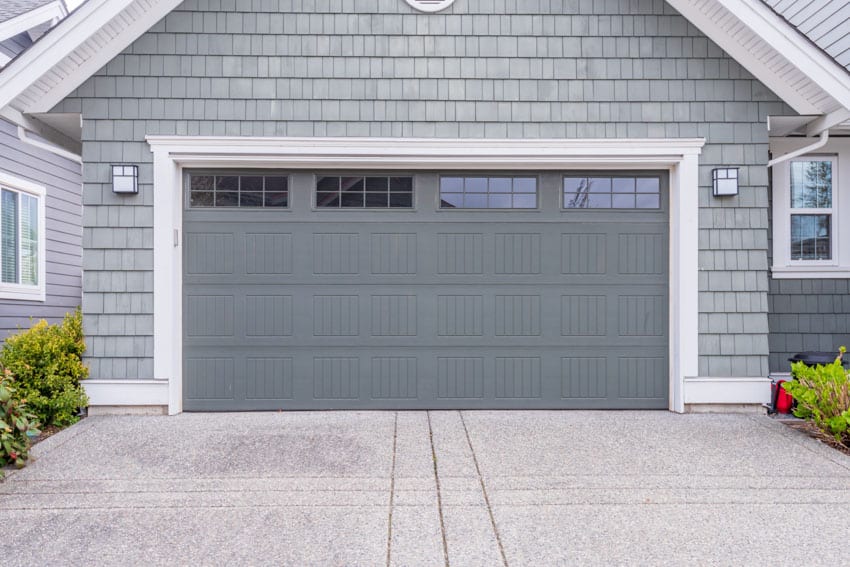 Detached garage with tinted windows, garage door, wall mounted lights, and concrete driveway