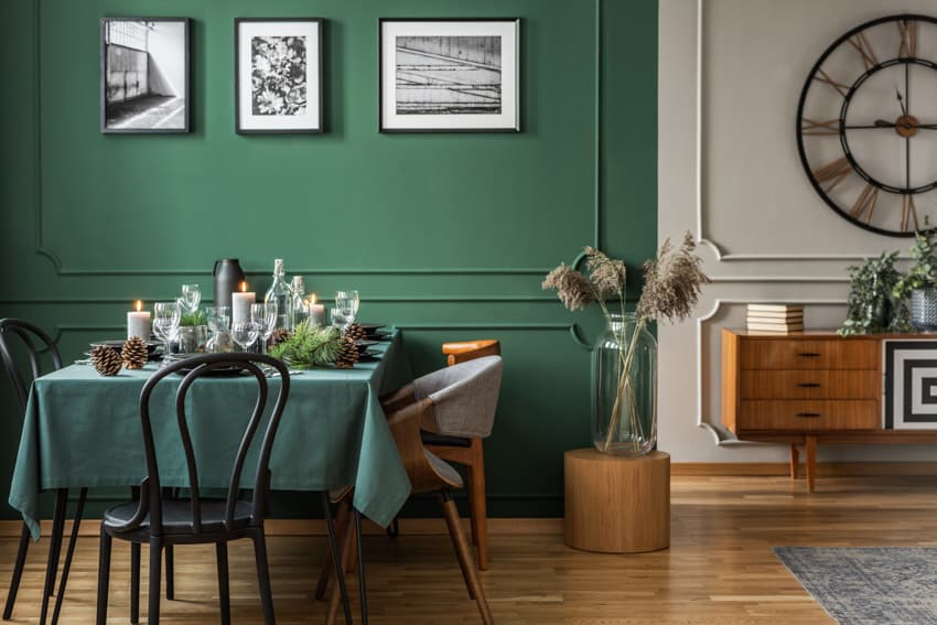 Dining room with green backdrop, dining table, chairs, vase, and wood flooring