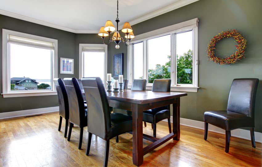 Green dining room with wood table, chairs, wooden flooring, chandelier, and windows