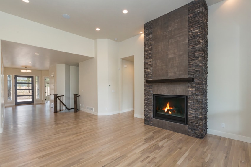 Empty living room with black ledger stone fireplace, wood flooring, white walls, and ceiling lights