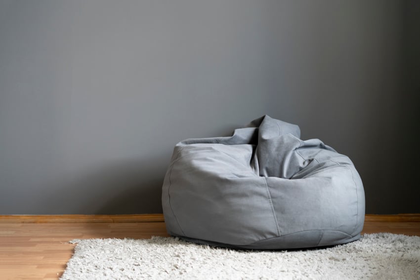 Empty room with adult bean bag chair, gray wall, wood floor, and rug