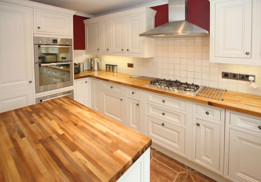 Farmhouse kitchen with cedar countertops, white cabinets, square tile backsplash, stove, and range hood