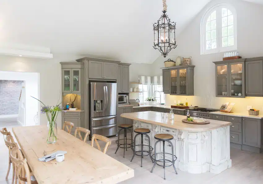 Farmhouse kitchen with bronze chandelier, bar stools, gray cabinets, and rustic whitewashed island,