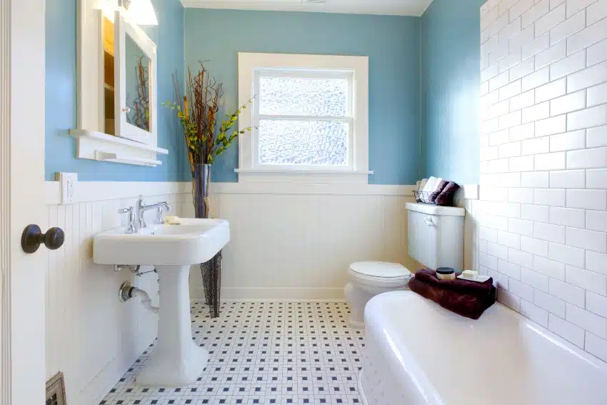 Fresh looking bathroom with white and blue tones features subway tiles on the wall, bathtub and narrow pedestal sink
