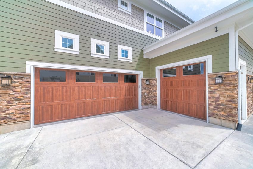 Garage with concrete driveway, wooden doors, siding, stone wall cladding, and tinted window covering