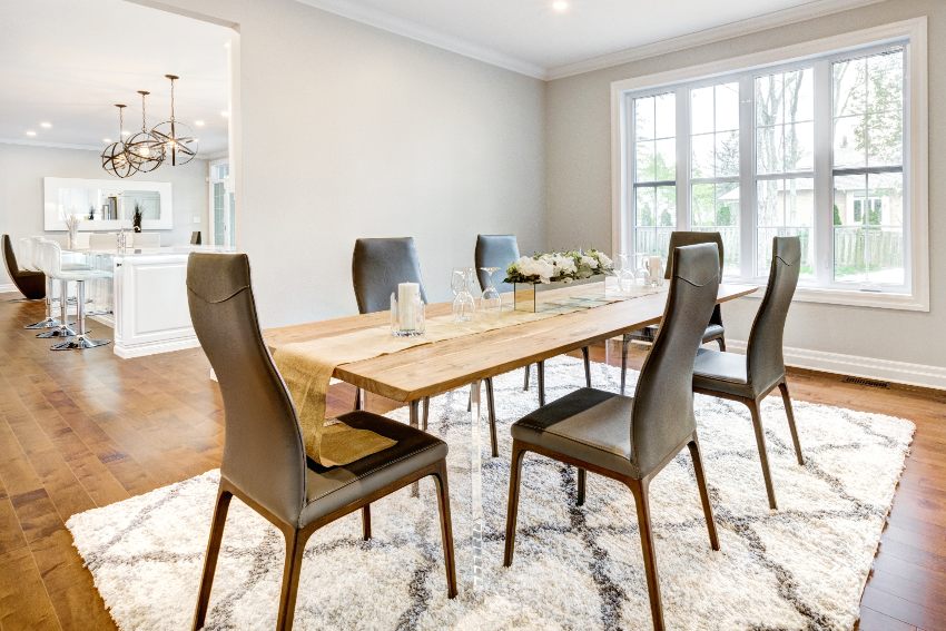 Gorgeous dining room with grey and beige tones features chestnut wood dining table with grey chairs and carpet on wooden floors