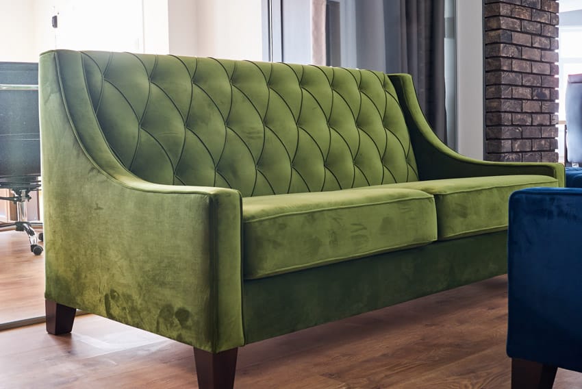 Tifted green velvet couch, grey curtains and brick columns