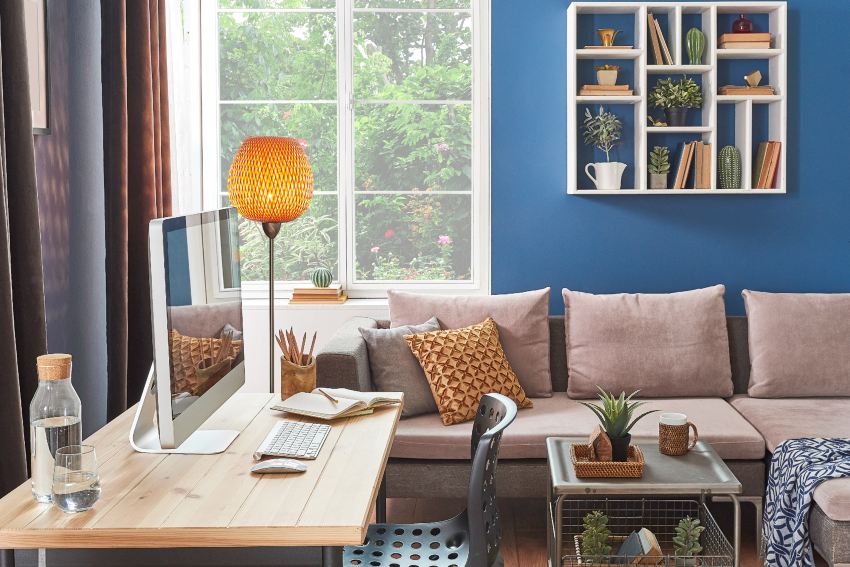 Home office features blue accent wall with book shelf, sofa, coffee table and working desk with computer