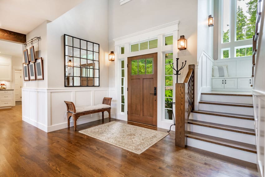 Foyer with wood door, entry mat, bench, staircase, and wall sconces