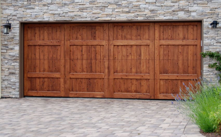 House exterior with wooden bifold garage doors, driveway, and stone wall cladding